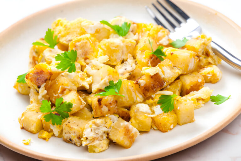 A close-up view of a plate of scrambled eggs mixed with diced potatoes and garnished with fresh parsley.