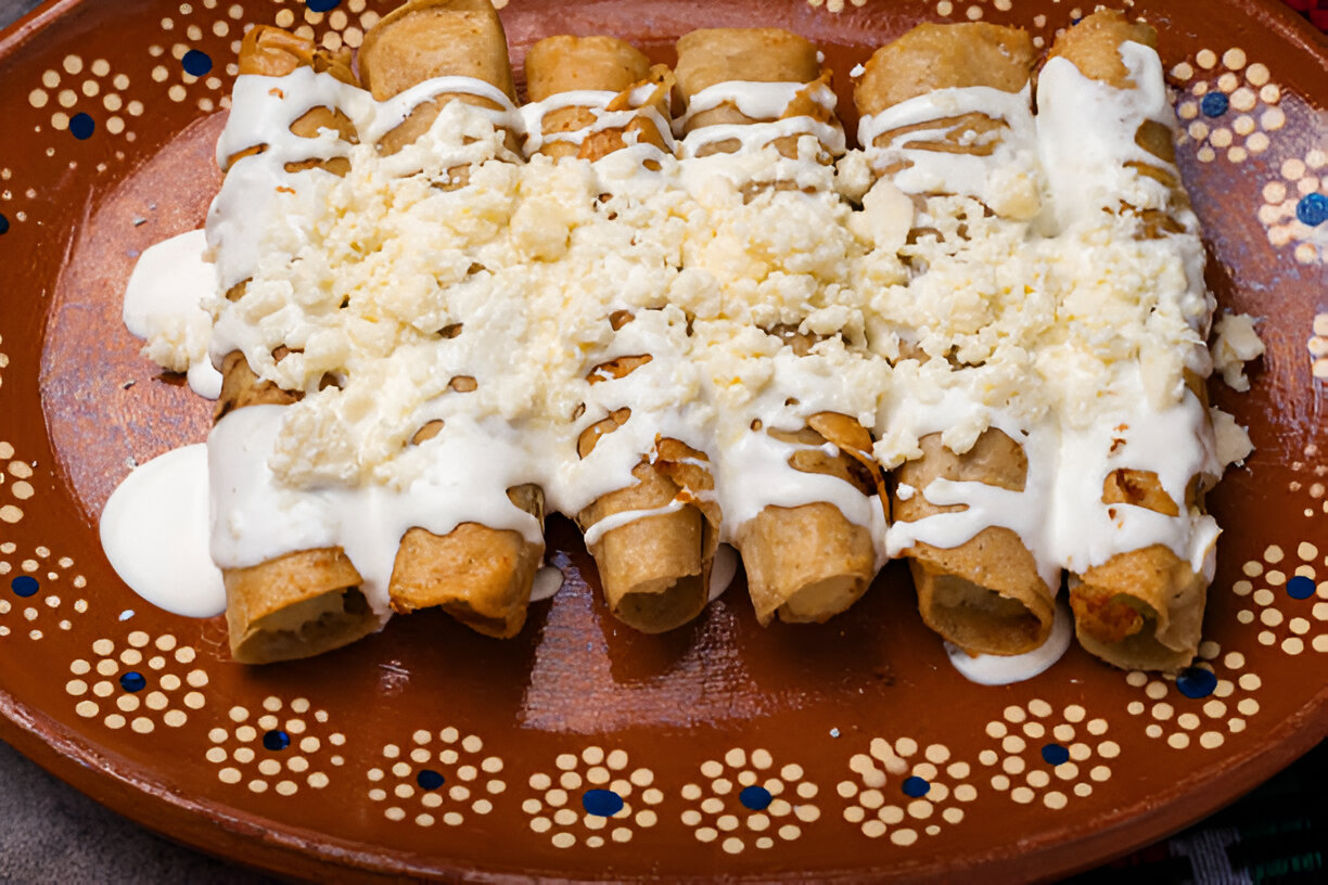 A plate of freshly made taquitos topped with cream and crumbled cheese.