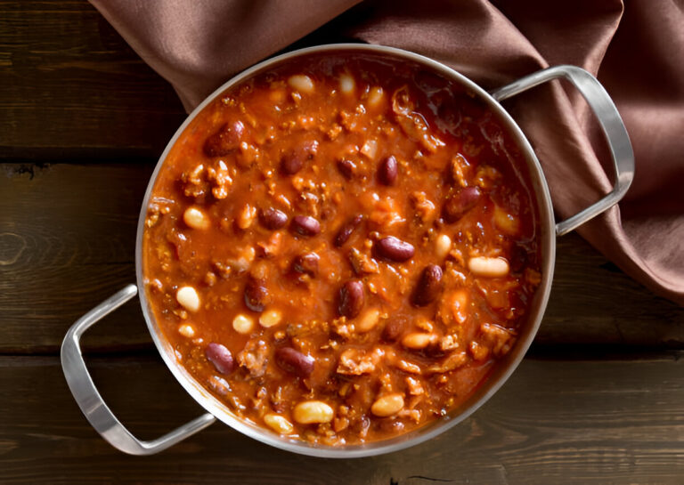 A pot of chili with various beans and ground meat on a wooden table.