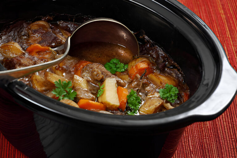 A close-up view of a hearty beef stew in a black slow cooker, garnished with fresh parsley.