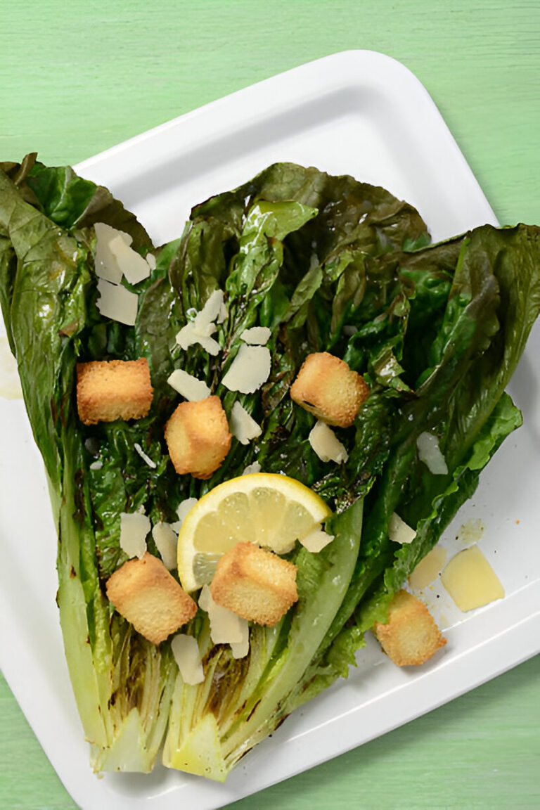A fresh romaine lettuce with croutons, lemon slices, and shaved cheese on a white plate