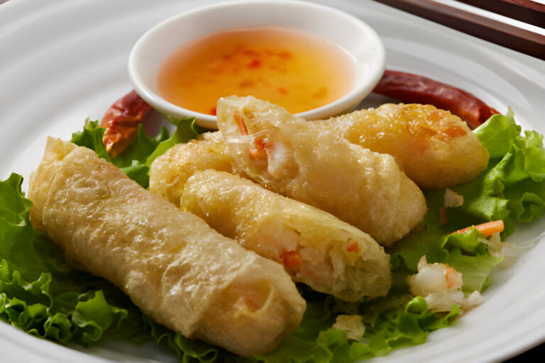 Plate of crispy spring rolls served with a small bowl of dipping sauce on a bed of lettuce.