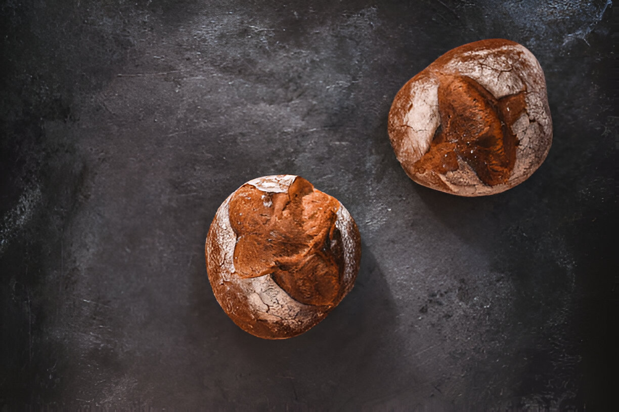 Two round rustic loaves of bread on a dark surface.