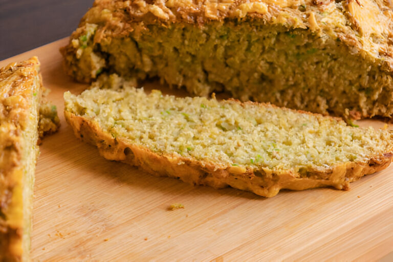 Freshly baked zucchini bread with a golden crust, sliced on a wooden cutting board.